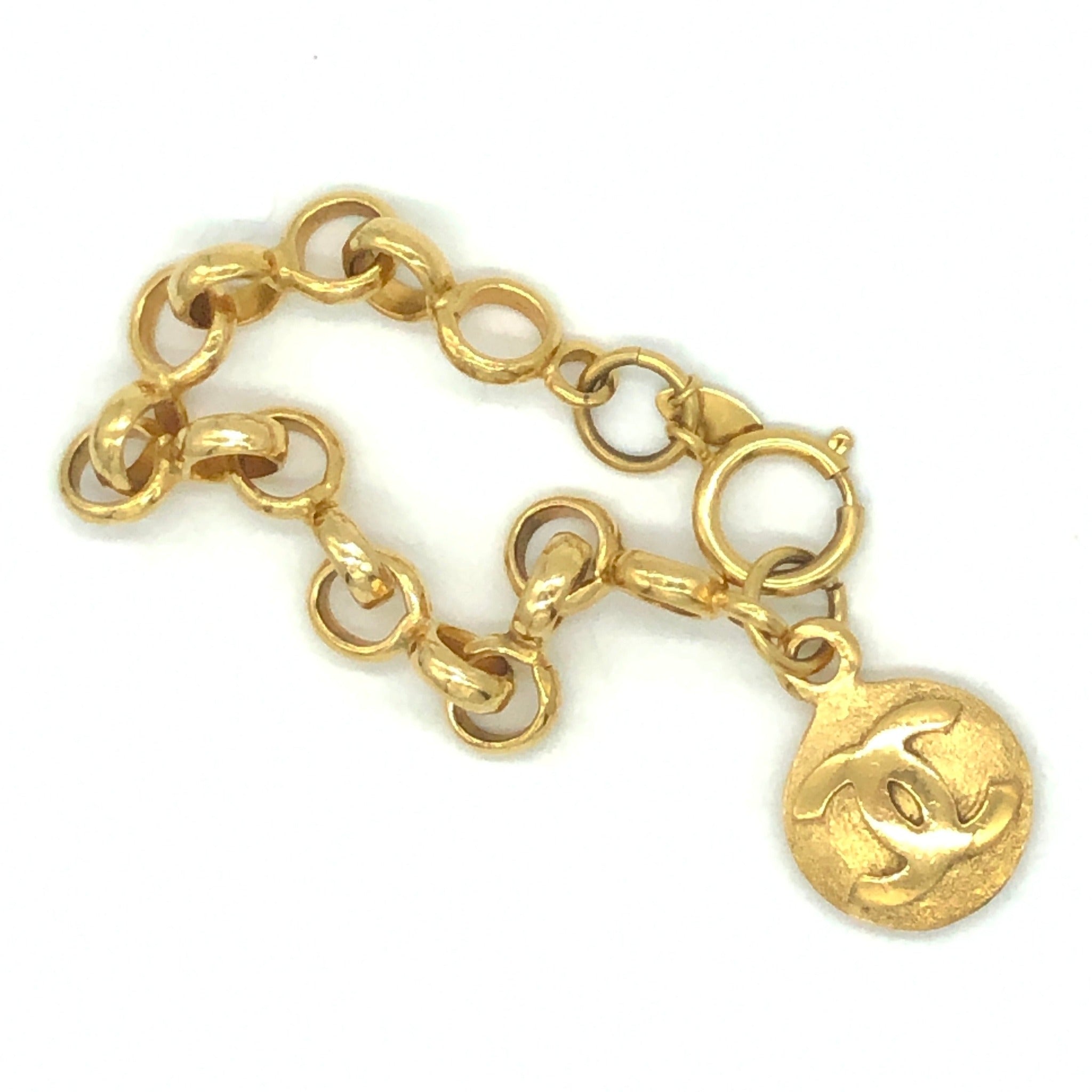 Lot - Chanel gold hinged bangle bracelet with embossed C.H.A.N.E.L. and a  safety chain, signed 'Chanel Made In France,' 1980s.